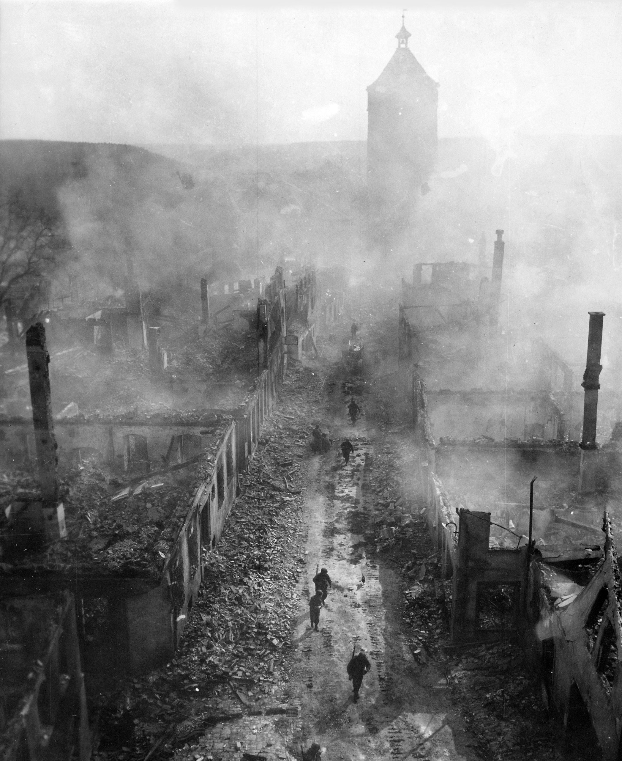 Black and white image of soldiers moving through a bombed-out, smoky city